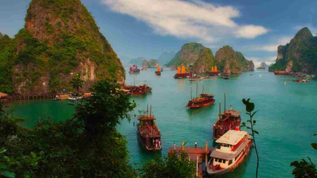 BAHÍA DE HALONG, viaje de vietnam en familia. Bahía con tonos turquesa y pequeña embarcación. Piedras al fondo.