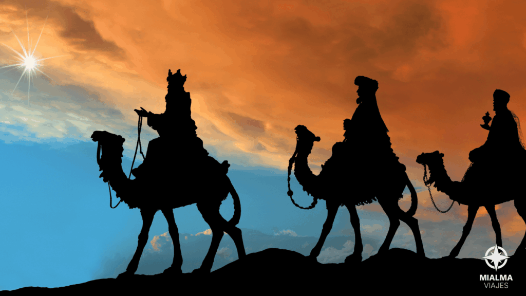 Fotografía de tres hombres (los Tres Reyes Magos) montados en camello siguiendo una estrella del cielo, mientras cruzan el desierto. Esquina derecha inferior logo de Mialma Viajes, agencia de viajes en familia. 