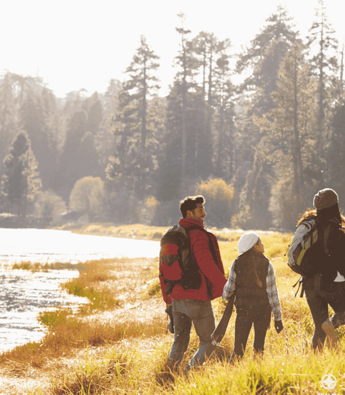 Fotografía de familia caminando en el margen del río con bosque de fondo. Logo de Mialma Viajes en esquina inferior derecha.