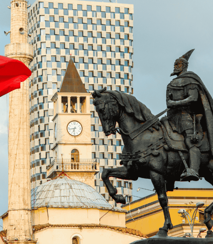 Fotografía de la plaza Skanderbeg en Tirana Albania. Plano directo a la estatua de Skanderbeg y a la bandera de Albania. De fondo se ven edificios propios de la ciudad