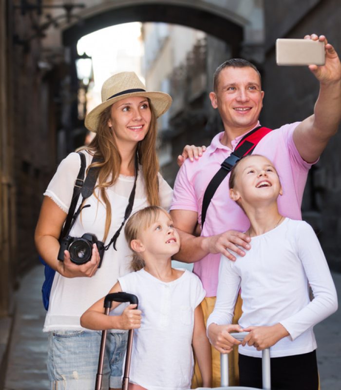 Positive parents with two kids taking selfie near city sights